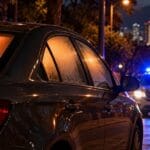 Carro estacionado de noche con las ventanas empañadas mientras se acerca una patrulla
