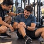 Hombre lesionado en un gimnasio recibe ayuda de un entrenador